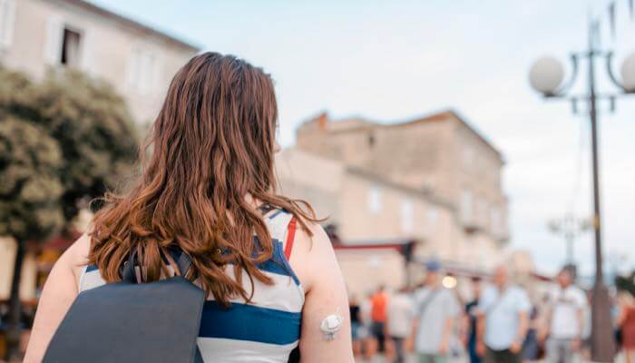 Woman With CGM on Arm Back view of woman outdoors with a CGM on her upper arm & wearing a backback