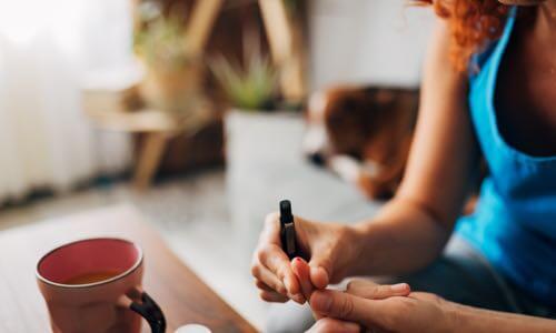 Woman sitting at desk squeezing her finger after using lancing device to test blood sugar