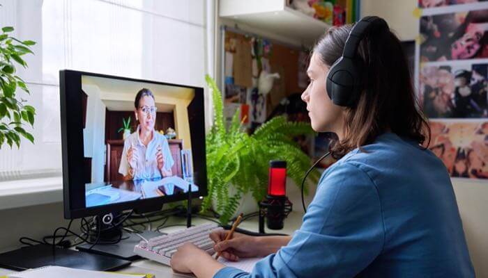 Young woman sitting at a desk wearing a headset & having a virtual meeting on her desktop computer