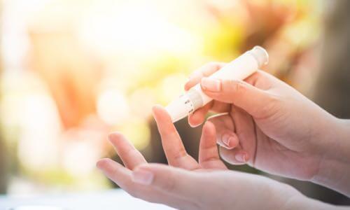Female hand holds a BGM lancing device while pricking her finger on the other hand