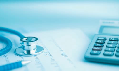 Stethoscope at left & calculator at right laying on top of a document on desk