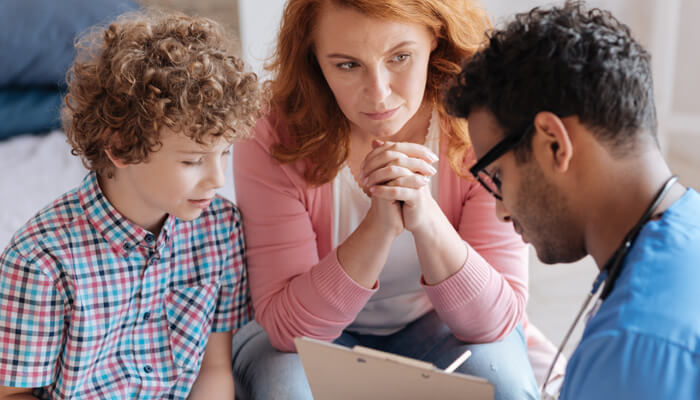 Mother and son watch as a male health care professional writes on his medical clipboard